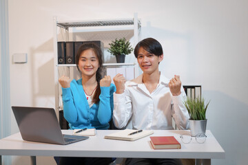 An Asian male consultant and an African American female intern sit at a table with laptops doing paperwork together to discuss a project's financial reports. Company business collaboration concept