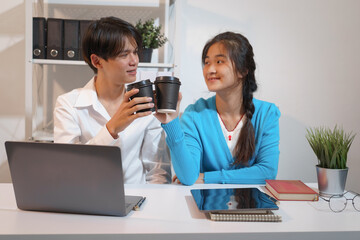 An Asian male consultant and an African American female intern sit at a table with laptops doing paperwork together to discuss a project's financial reports. Company business collaboration concept