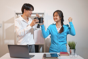 An Asian male consultant and an African American female intern sit at a table with laptops doing...