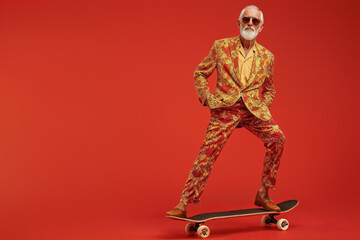 Senior man in formal suit skateboarding, red backdrop