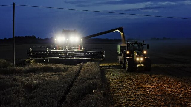 Combine harvester and tractor loading off crop in the field at night