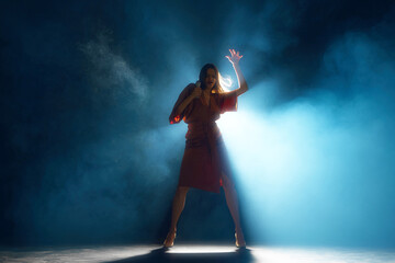 Woman, vocalist in moment of passion, highlighted by backlight and theatrical smoke on stage...