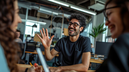 Fototapeta na wymiar Young man with an afro hairstyle and glasses is smiling and giving a high-five in a casual office or coworking space environment.