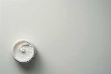Background with copy space featuring an open jar of white face cream on a clean, bright surface, providing a minimalist setting for skincare branding.