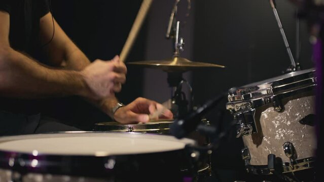 A young Caucasian man drummer plays a drum kit in a music studio. Creates music and art. Drum set, drum kit in dark, drummer plays. The rock band is rehearsing, studying. The musician is playing
