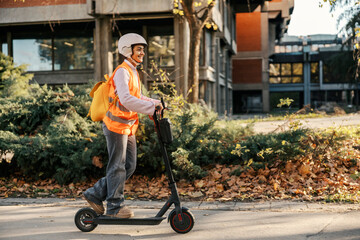A happy girl is driving an electric scooter while wearing vest and helmet on the street. © Dusan Petkovic
