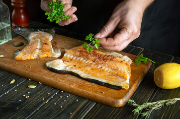Cooking fish steaks. The cook adds aromatic herbs to the salmon fish with his hands before baking.
