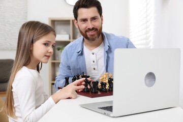Father teaching his daughter to play chess following online lesson at home