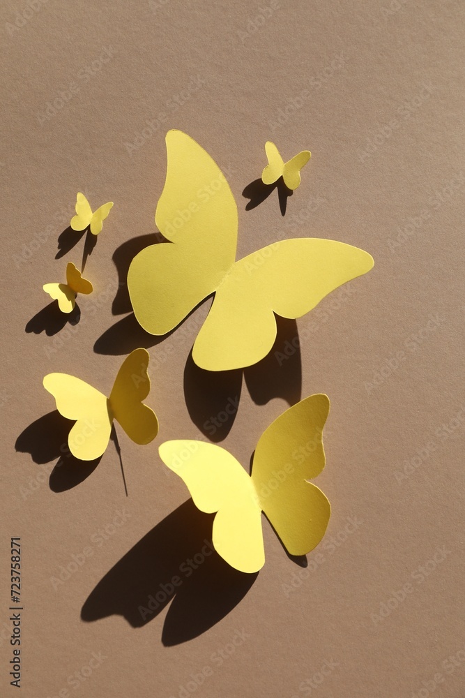 Poster Yellow paper butterflies on light brown background, top view