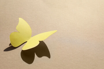 Yellow paper butterfly on light brown background, space for text © New Africa