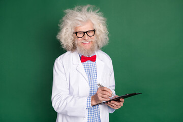 Photo of cute cheerful age scientist wear white coat bowtie spectacles writing papers smiling isolated green color background
