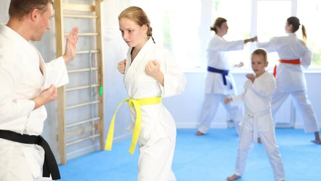 Teen girl is paired with male teacher to learn how to strike and rehearses blocking opponent, using karate technique