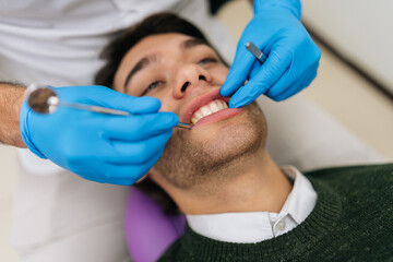 Closeup face of young man patient at dentist chair during dental procedure. Close-up hands of...