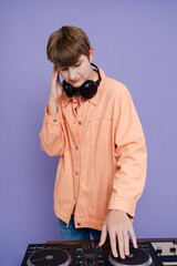 Cheerful DJ teenager playing and listening music on a color background.