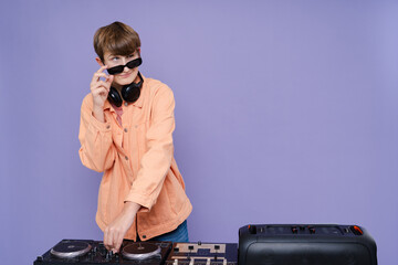 Cool charming boy with headphone and sunglasses play music on a turntable isolated over bright color background