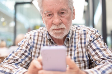 Serious concentrated senior bearded man sitting indoor using mobile phone, old people and new technologies