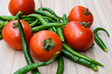 Red tomato and green chili pepper on plain wooden table, green essential vegetables for all essential foods, view of unpeeled vegetables with plain background