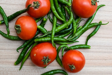 Red tomato and green chili pepper on plain wooden table, green essential vegetables for all essential foods, view of unpeeled vegetables with plain background