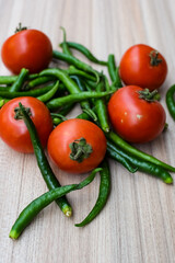 Red tomato and green chili pepper on plain wooden table, green essential vegetables for all essential foods, view of unpeeled vegetables with plain background