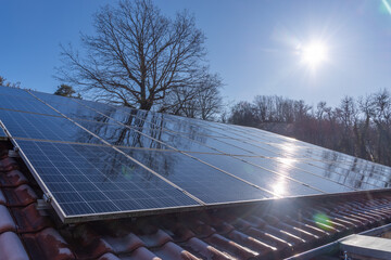 Solarmodule auf einem Hausdach reflektieren die Winter Sonne vor einem klaren blauen Himmel,...