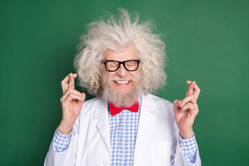 Photo of happy funky funny smiling crazy mad scientist with crossed fingers anticipation isolated on green color background