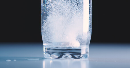 Painkiller tablet in glass of water and dissolves strongly bubbling on floor, close-up, black...