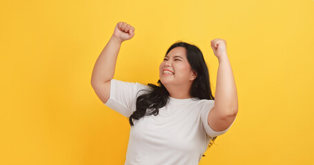 A chubby Asian woman wearing a white t-shirt showing very happy expression on a yellow background.