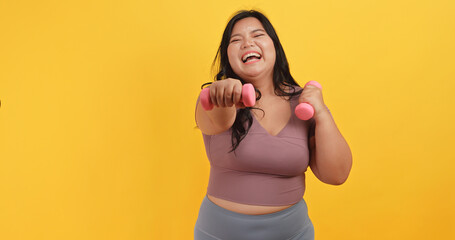 A chubby Asian woman wearing exercise clothes is showing off her physical strength on a yellow background.
