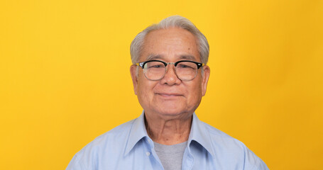 Close up, portrait of older man smiling and looking at the camera. Isolated on yellow background in...