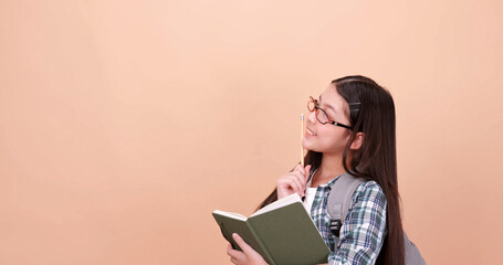 Schoolgirl thinking something and write it down in a notebook. Isolated on brown background in studio.