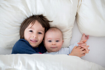 Two children, baby and his older brother in bed in the morning, playing together, laughing and having a good time