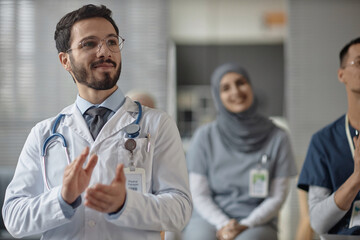 Waist up shot of cheerful Muslim man doctor complimenting speaker with applause at medical conference - obrazy, fototapety, plakaty