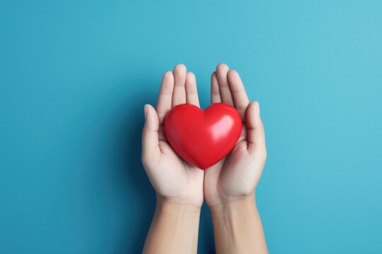 A person holds a red heart in their hands. This image can be used to convey love, care, and affection