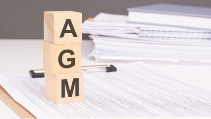 text agm - Annual General Meeting - on wooden blocks. the background is a business papers. finance concept. white background