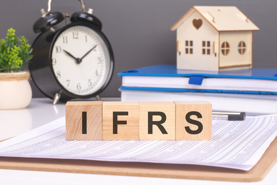 ifrs word in wooden blocks with small wooden house and alarm clock on background. idea of incorporating International Financial Reporting Standards into the foundation of business operations