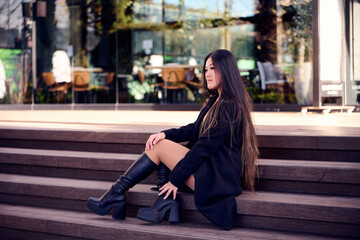 Fototapeta premium Portrait of a beautiful young Asian woman in a black coat and boots 