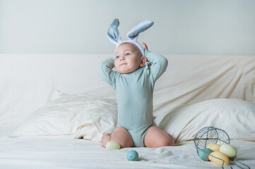 Baby girl 1 year old on bed with basket and Easter eggs. Egg hunting, kids activity