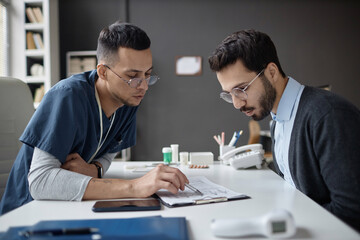 Medium shot of Islamic male physician and patient at table looking at medical questionnaire in hospital