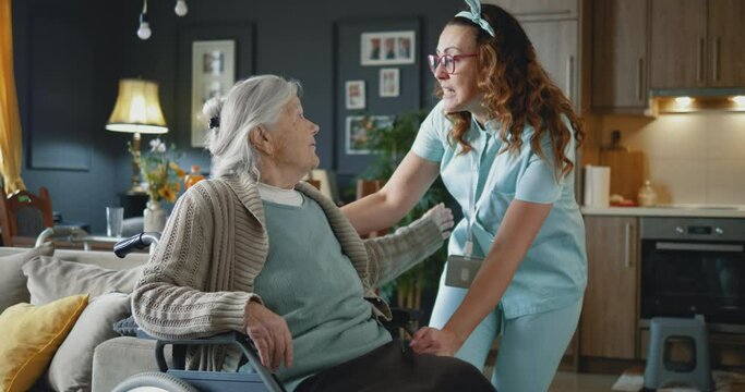 Woman in medical uniform home caregiver takes care of old disabled woman at home,.