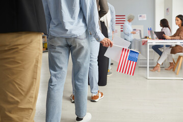 Cropped photo of a group of unrecognizable american citizens people standing in polling station. Voters standing in a queue at vote center getting ballot paper. Election day concept. - obrazy, fototapety, plakaty
