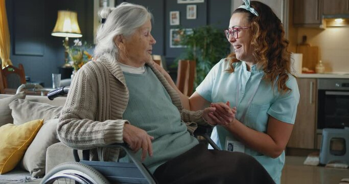 Senior woman in wheelchair and nurse caregiver with holding hands, talking, support and care in retirement at home