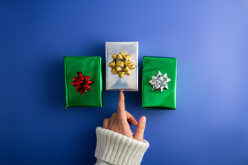 First person top view photo of female hands holding three shiny green and silver gift boxes with bow on isolated blue background.