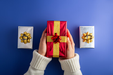 First person top view photo of female hands holding shiny red gift box over silver surprise boxes...