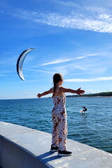 A girl stands on the seashore with her arms open and admires a man who rides across the sea on a board with a parachute - kitesurfing, kiting, kite