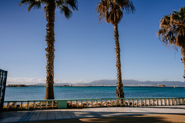 Santa Margarita, Spain - January 24, 2024 -  palm trees by a blue balustrade overlooking a sea with distant mountains and a clear blue sky.
