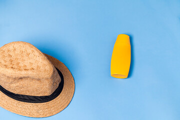Straw hat on blue background with bottle of sunscreen. View from above. Beach concept. Summer concept.