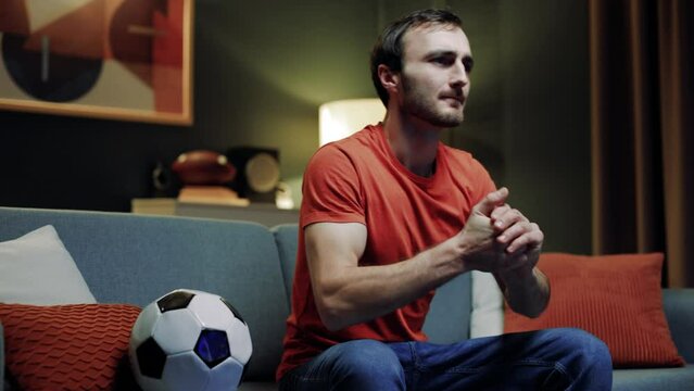 Handsome bearded man sitting alone in living room, football fan loving soccer cheering on football team on couch. Sports enthusiast unwinding in evening while watching sports station on television.