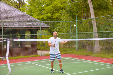 man plays badminton outdoors in the fresh air, throws a shuttlecock and holds a racket, an island in the Maldives, active recreation and sports