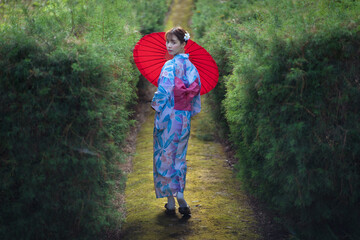 Pretty girl in a Yukata dress.  Portrait fashion young Asian women wearing a traditional Japanese kimono or Yukata dress and holding a red umbrella are happy and relaxing in the fresh green nature.