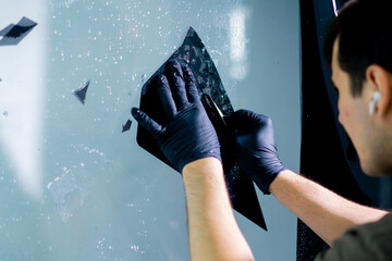 the mechanic cuts off excess pieces of tinting protective film with a clerical knife detailing - obrazy, fototapety, plakaty
